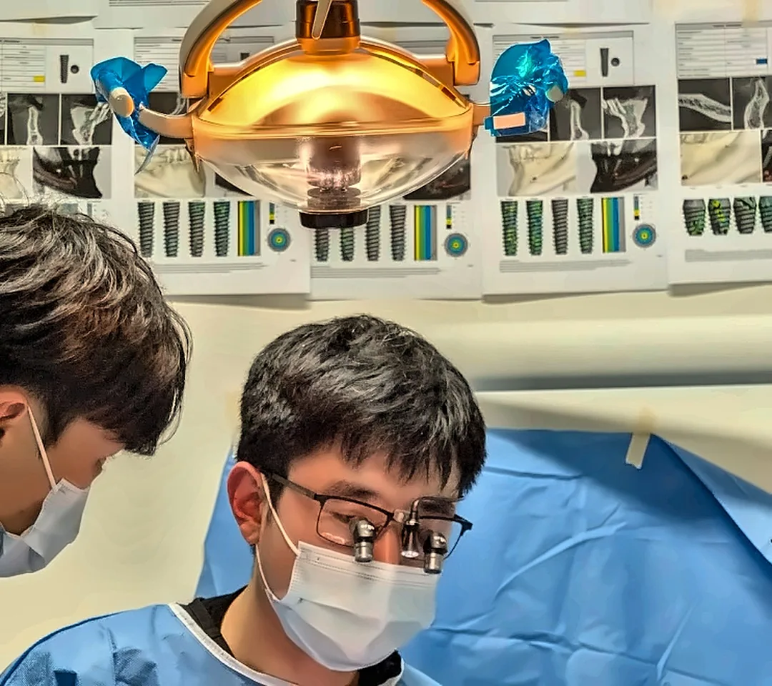Dr James Lee performing guided implant surgery at Park Road Dental, with 3D planning printouts on the wall.
