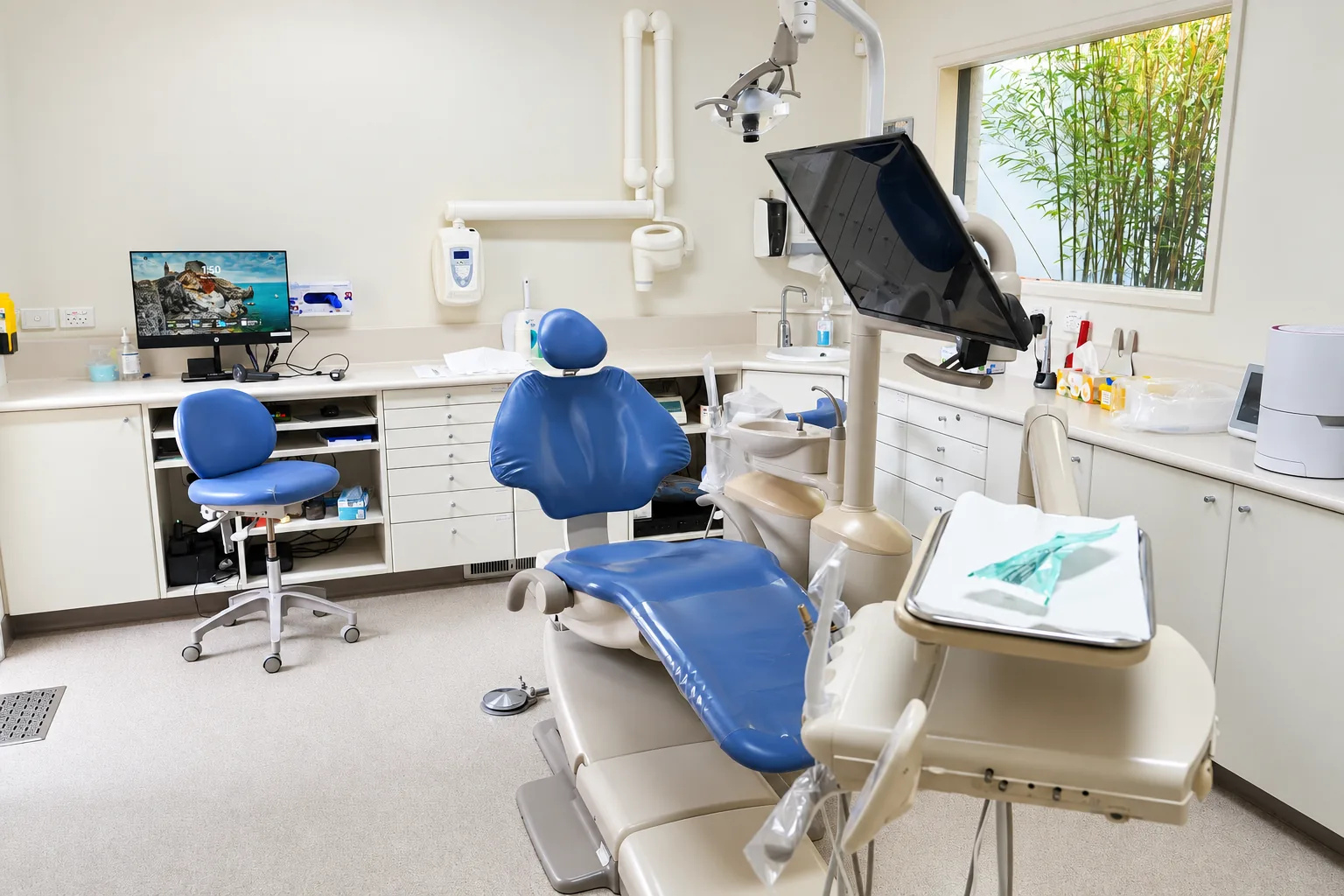 A treatment room at Park Road Dental with a blue dental chair, overhead light and a window onto bamboo in the garden